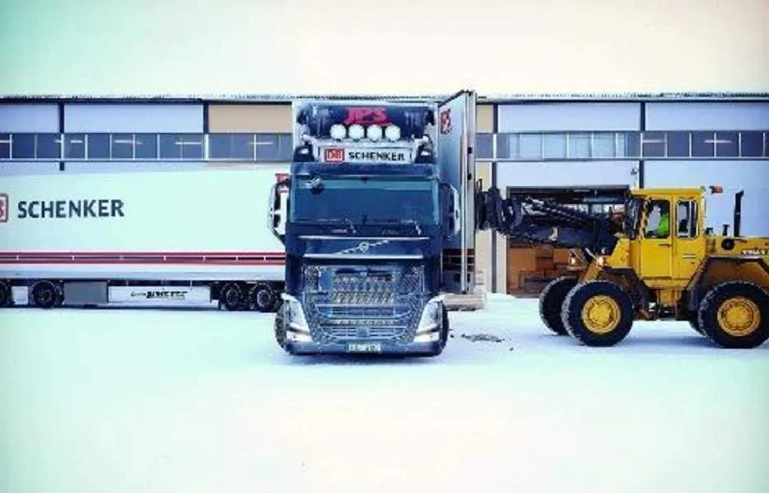 Blå Volvo med skåp och en hjullastare framför verkstadsportarna.