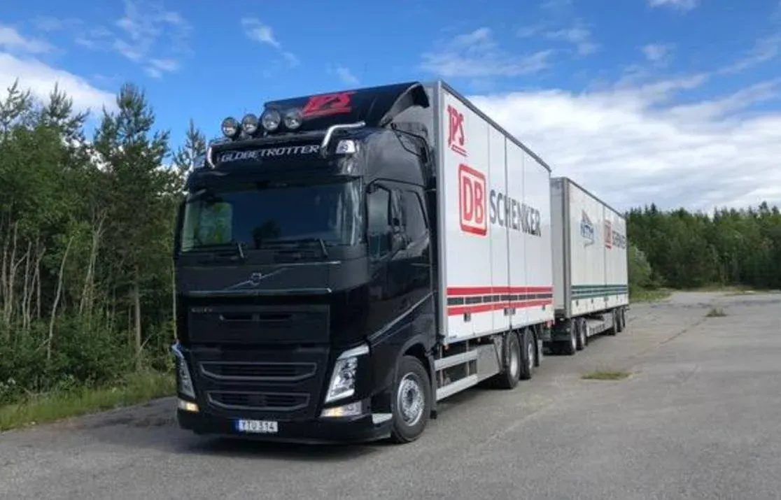 Svart Volvo dragbil med skåp på grusplan omgiven av skog.